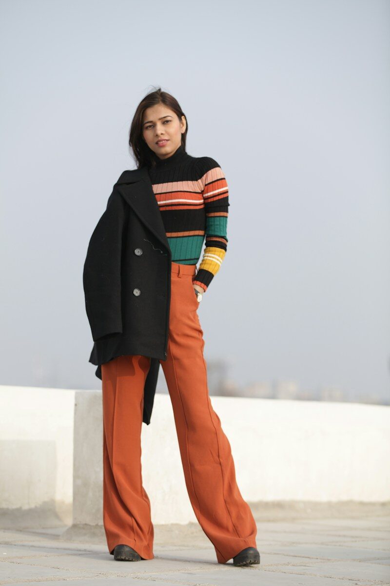 woman in black coat and orange pants standing on white concrete wall during daytime